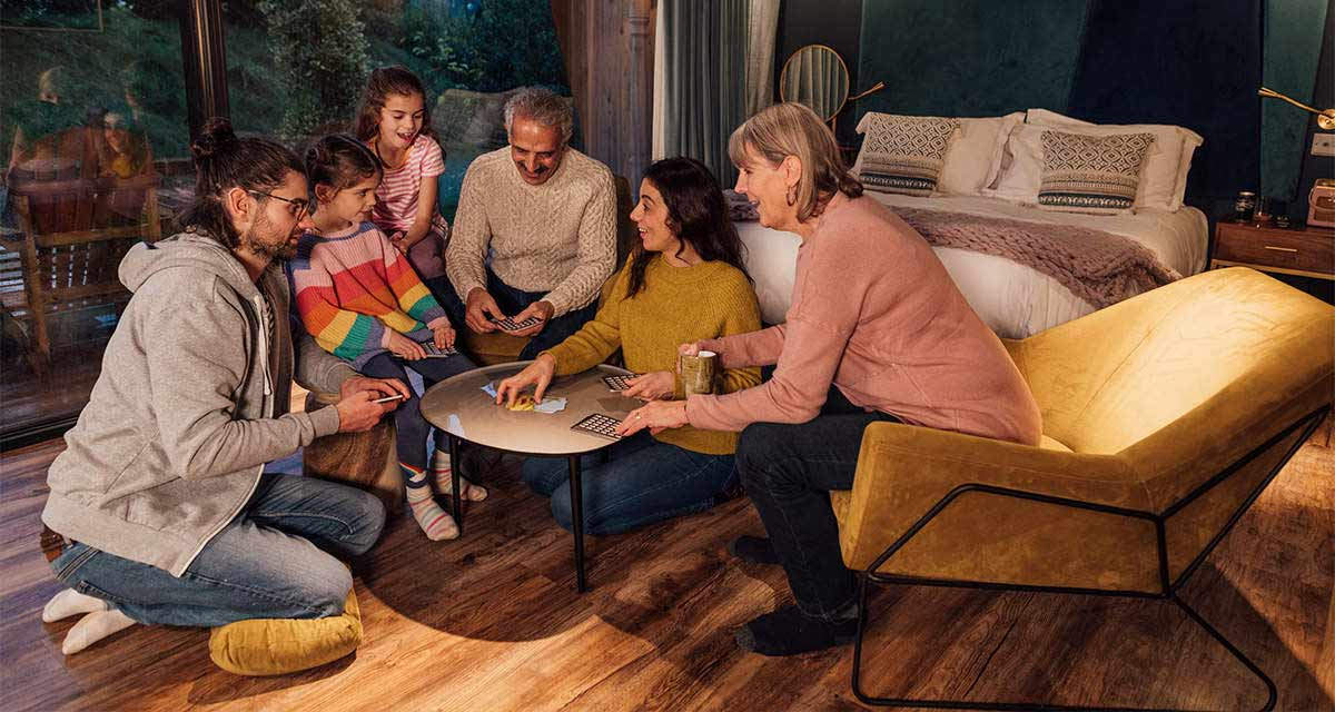 Una famiglia, con i nonni, gioca intorno a un tavolo in un soggiorno.
