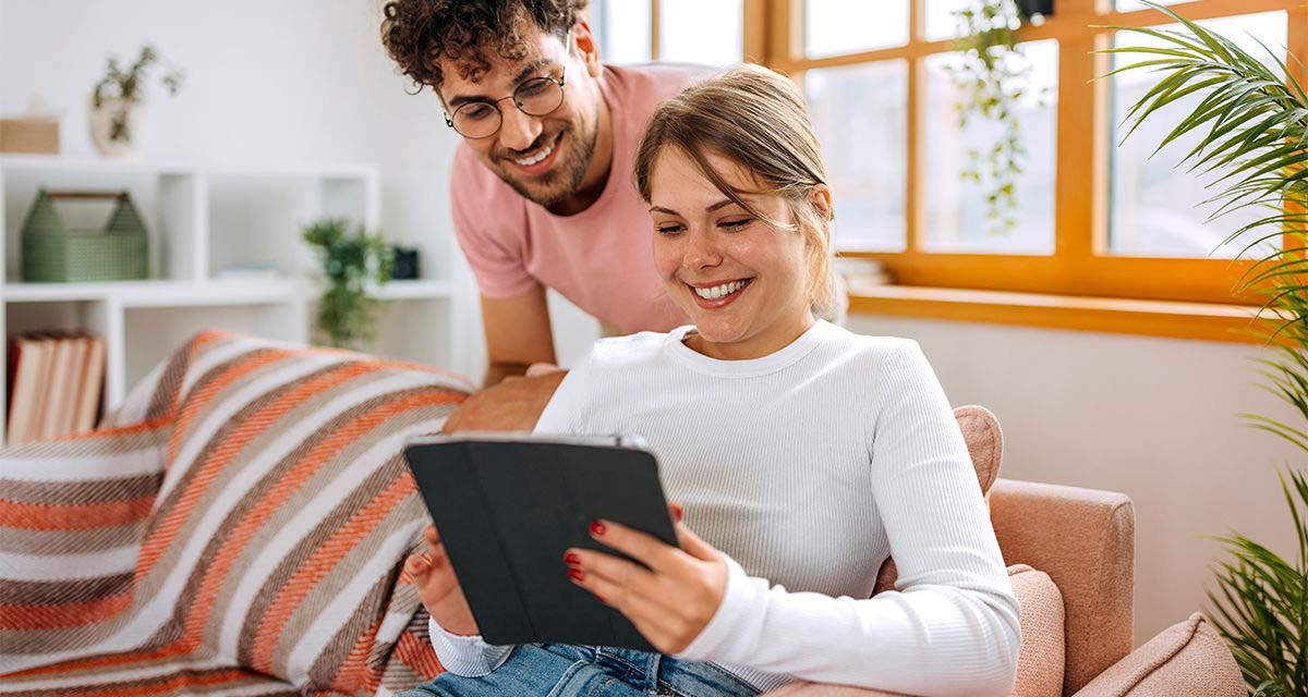 Una giovane coppia con un tablet in soggiorno: tenere sotto controllo le utenze, come il gas, è importante per il risparmio domestico