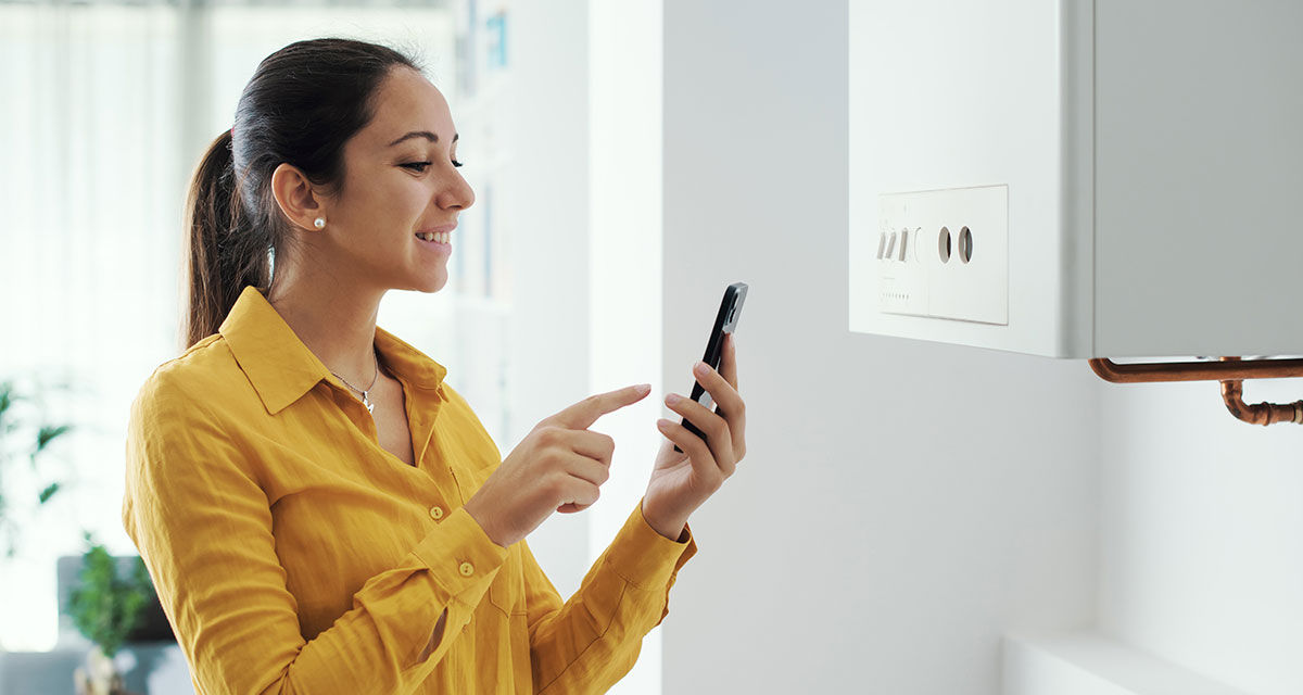 Una ragazza regola con lo smartphone il clima domestico: la gestione a distanza è un criterio per scegliere la caldaia