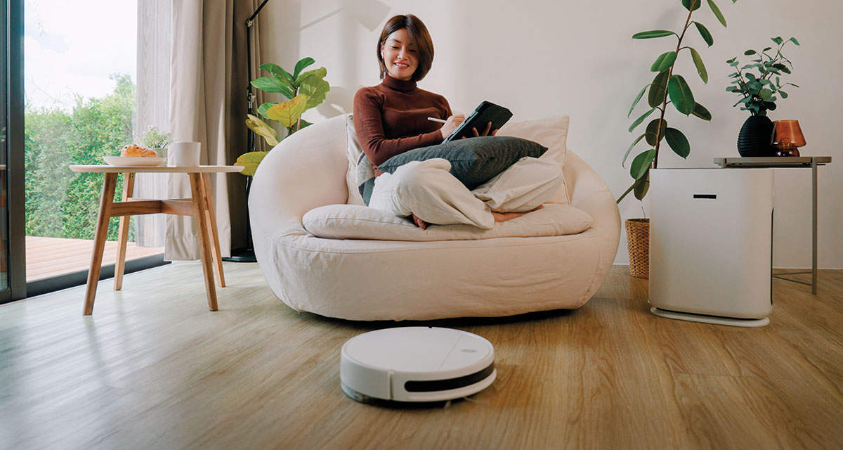Una giovane donna si rilassa mentre osserva un’aspirapolvere senza fili collegato all’impianto domotico