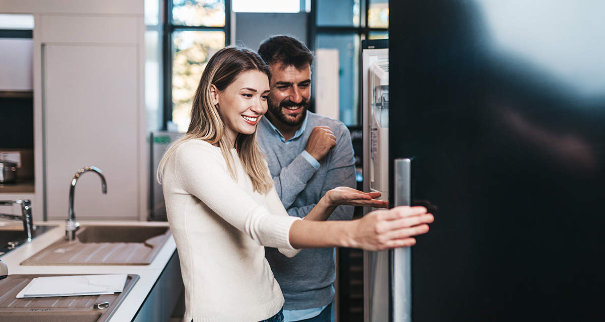 Una giovane coppia accanto a un frigorifero, uno degli elettrodomestici che consumano di più